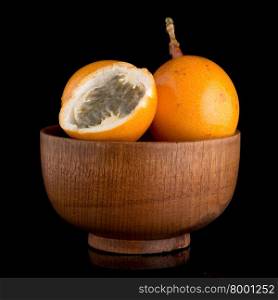 Passion fruit maracuja granadilla on wooden bowl, black background.