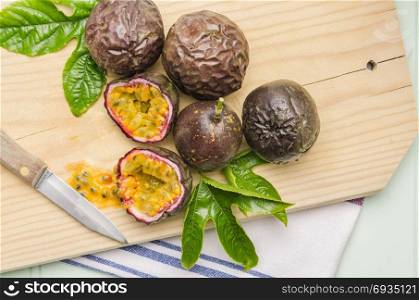 Passion fruits with leaves and knife on the vintage wooden table.