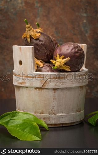 Passion fruits with leaves on a white painted wooden bucket on the vintage metal textured background.