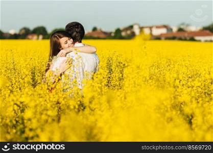 Passionate affectionate couple embrace each other, miss very much as haven t seen for long time, spend wonderful summer day outdoor in yellow field. Romantic female and male hug with great love