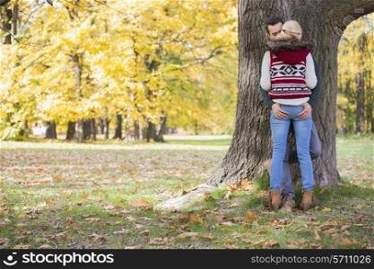 Passionate couple against tree trunk in park during autumn