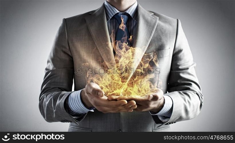 Passionate for power. Young businessman holding fire flames in palms