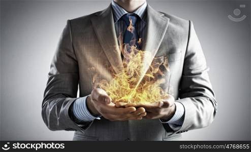 Passionate for power. Young businessman holding fire flames in palms