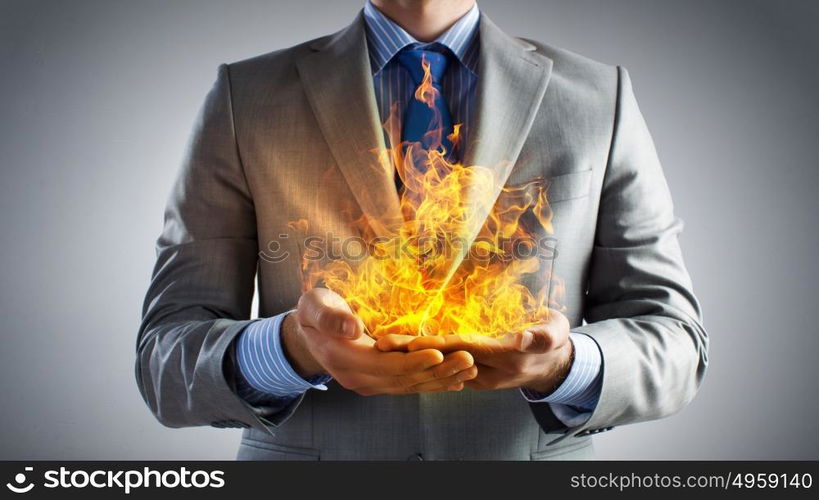 Passionate for power. Young businessman holding fire flames in palms