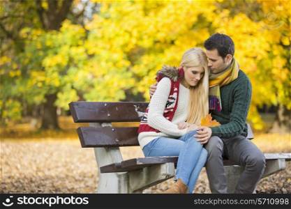Passionate young man hugging shy woman on park bench during autumn