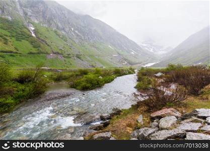 Passo del San Gottardo or St. Gotthard Pass summer misty landscape with water stream (Switzerland). Rainy weather.