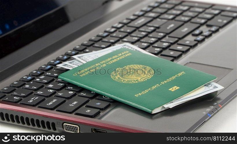 Passport of Uzbekistan with US dollars on laptop keyboard. Online registration. Concept - briber and corruption. Passport of Uzbekistan on the keyboard