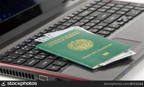 Passport of Uzbekistan with US dollars on laptop keyboard. Online registration. Concept - briber and corruption. Passport of Uzbekistan on the keyboard