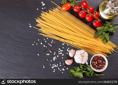 Pasta and cooking ingridients on black slate surface. Spaghetti, tomato, olive oil, spice, garlic and parsley. Italian cuisine concept. Top view, flat lay, mockup with copy space for text. Pasta and cooking ingredients on black slate background.