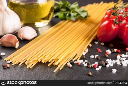 Pasta and cooking ingridients on black slate surface. Spaghetti, tomato, olive oil, garlic, parsley and spices. Italian cuisine. Pasta and food ingredients on black background.