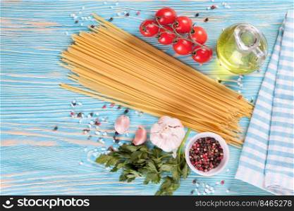 Pasta and cooking ingridients on blue wooden surface. Spaghetti, tomato, olive oil, spice, garlic and parsley. Italian cuisine concept. Top view, flat lay, mockup with copy space for text. Pasta and cooking ingredients on blue wooden background.
