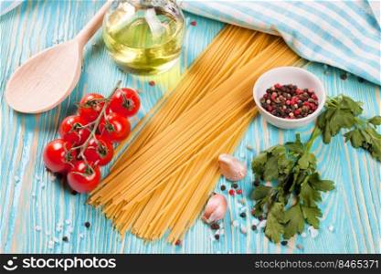Pasta and cooking ingridients on blue wooden surface. Spaghetti, tomato, olive oil, spice, garlic and parsley. Italian cuisine concept. Top view, flat lay. Pasta and cooking ingredients on blue wooden background.