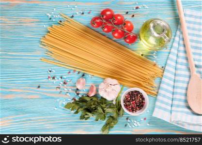 Pasta and cooking ingridients on blue wooden surface. Spaghetti, tomato, olive oil, sπce, garlic and pars≤y. Italian cuisi≠concept. Top view, flat lay, mockup with©space for text. Pasta and cooking ingredients on blue wooden background.