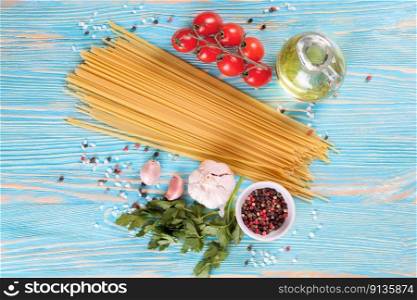 Pasta and cooking ingridients on blue wooden surface. Spaghetti, tomato, olive oil, spice, garlic and parsley. Italian cuisine concept. Top view, flat lay. Pasta and cooking ingredients on blue wooden background.