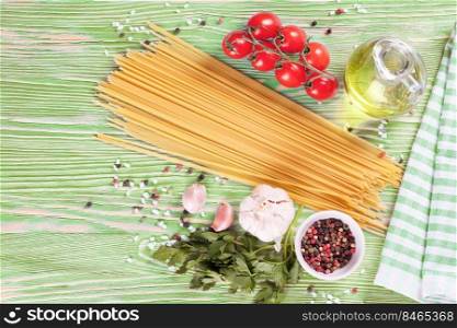 Pasta and cooking ingridients on green wooden surface. Spaghetti, tomato, olive oil, spice, garlic and parsley. Italian cuisine concept. Top view, flat lay, mockup with copy space for text. Pasta and cooking ingredients on green wooden background.