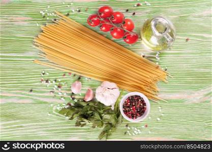 Pasta and cooking ingridients on green wooden surface. Spaghetti, tomato, olive oil, spice, garlic and parsley. Italian cuisine concept. Top view, flat lay. Pasta and cooking ingredients on green wooden background.