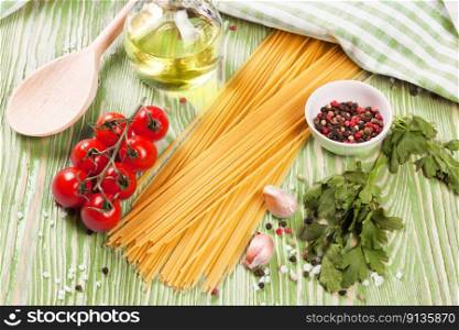 Pasta and cooking ingridients on green wooden surface. Spaghetti, tomato, olive oil, spice, garlic and parsley. Italian cuisine concept. Top view, flat lay. Pasta and cooking ingredients on green wooden background.