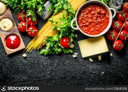 Pasta background. Dry spaghetti with Bolognese sauce,herbs, tomatoes and cheese. On black rustic background. Pasta background. Dry spaghetti with Bolognese sauce,herbs, tomatoes and cheese.
