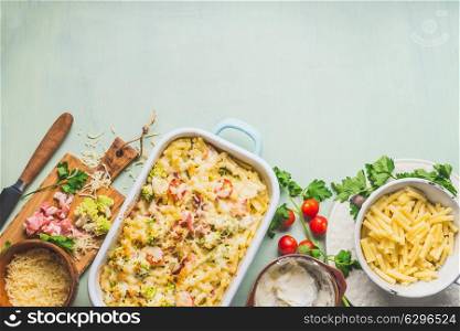 Pasta casserole with romanesco cabbage and ham in creamy sauce, on kitchen table background with ingredients, top view, border. Italian cuisine