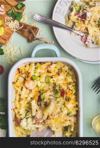 Pasta casserole with romanesco cabbage and ham in creamy sauce, served in plate with fork on kitchen table with ingredients, top view, close up. Italian cuisine