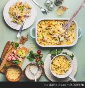 Pasta casserole with romanesco cabbage and ham in creamy sauce, served in plate with cutlery on kitchen table with ingredients, top view. Italian cuisine