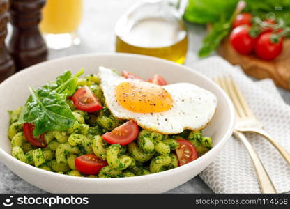 Pasta cavatappi with spinach pesto, tomatoes and fried egg in bowl served for lunch