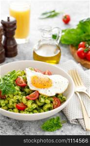 Pasta cavatappi with spinach pesto, tomatoes and fried egg in bowl served for lunch