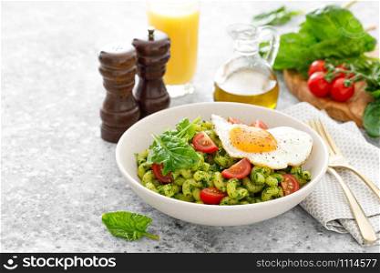 Pasta cavatappi with spinach pesto, tomatoes and fried egg in bowl served for lunch