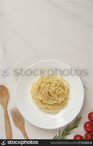 pasta concept a dish of boiled long slim pasta being served on the white tile table together with a wooden spoon and fork, tiny red tomato, and other ingredients.