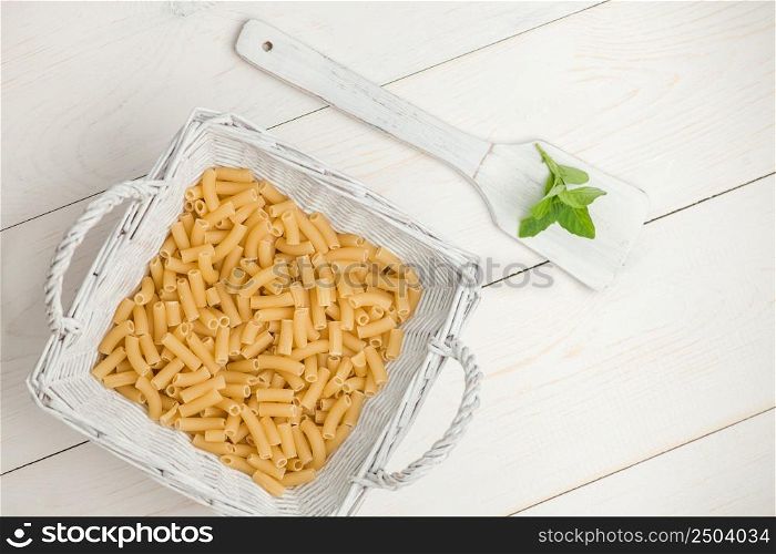 pasta in wicker basket and petals on the wooden spoon on white old wooden boards. pasta on white old table