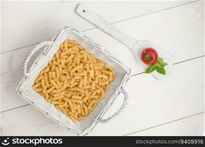 pasta in wicker basket and tomato on a wooden spoon on a white old wooden boards. pasta on white old table