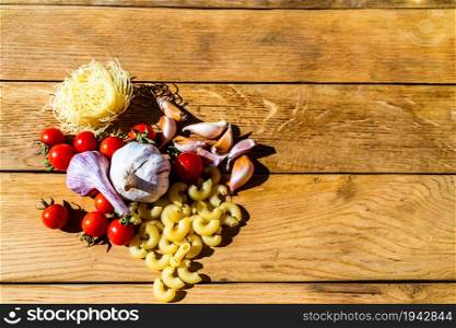 Pasta ingredients on wooden table. Cherry tomato, onion, garlic