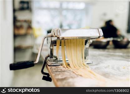 Pasta machine with dough on wooden kitchen table sprinkled with flour closeup, nobody. Traditional italian cuisine. Pasta machine with dough closeup, nobody
