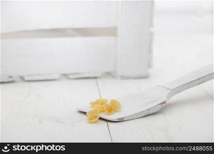 pasta on a wooden spoon and a box on a white old wooden boards. pasta on white old table