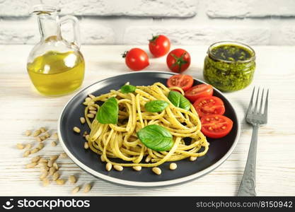 Pasta pesto with fork and fresh pesto sauce on white wooden background. Traditional italian spaghetti and food ingredients pesto sauce, tomato, parmesan, pine nuts, fresh basil leaves. Pasta with fresh homemade pesto sauce and food ingredients