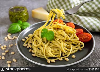 Pasta pesto with fork on grey concrete background. Traditional italian spaghetti with food ingredients pesto sauce, tomato, parmesan cheese, pine nuts, fresh basil leaves. Pasta with fresh homemade pesto sauce and food ingredients