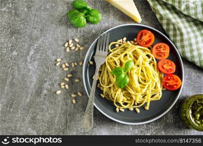 Pasta pesto with fork on grey concrete background. Flat lay with copy space. Traditional italian spaghetti and food ingredients pesto sauce, tomato, parmesan, pine nuts, fresh basil leaves. Pasta with fresh homemade pesto sauce and food ingredients