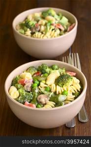 Pasta primavera with green asparagus, pea, broccoli, mushroom and tomato in cream sauce served in two bowls, photographed on dark wood with natural light (Selective Focus, Focus in the middle of the first bowl)