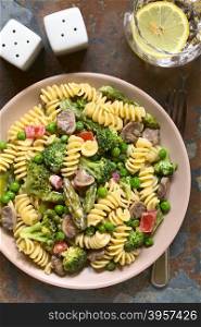 Pasta primavera with green asparagus, pea, broccoli, mushroom and tomato in cream sauce served on plate, photographed overhead on slate with natural light