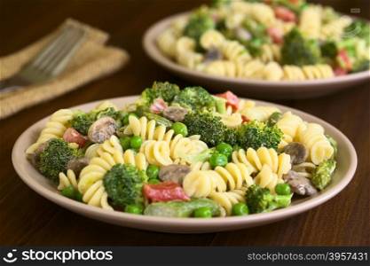 Pasta primavera with green asparagus, pea, broccoli, mushroom and tomato in cream sauce served on plates, photographed on dark wood with natural light (Selective Focus, Focus in the middle of the pasta on the first plate)