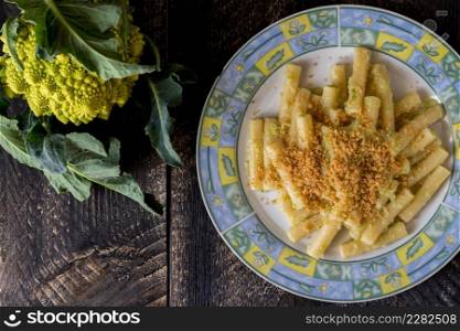 Pasta rigata with organic romanesco broccoli sauce and sprinkled with toasted breadcrumbs on black wooden background