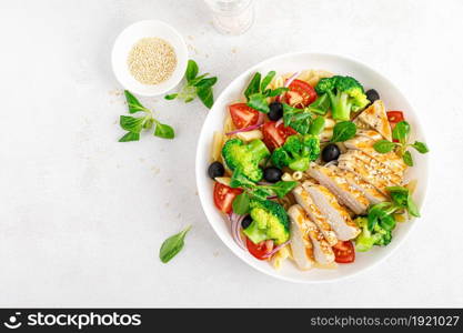 Pasta salad bowl with broccoli, tomato, onion, olives, corn salad and grilled chicken breast for lunch. Healthy dietary food. Top view.