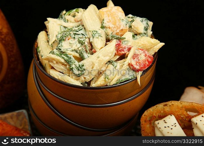 Pasta salad with spinach, red bell peppers, chicken, in bowl.