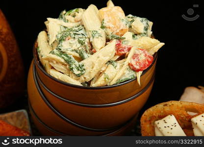 Pasta salad with spinach, red bell peppers, chicken, in bowl.