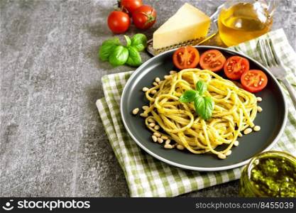 Pasta with fresh homemade pesto sauce on grey background with copy space. Traditional italian spaghetti with food Ingredients pesto sau e, tomato, parmesan cheese, pine nuts, fresh basil leaves. Pasta with fresh homemade pesto sauce and food ingredients