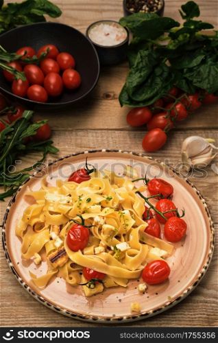Pasta with grilled cheese slices, frying cherry tomatoes and olive oil. Selective focus, vertical frame. Ingredients for spaghetti on a wooden table. Vegetarian pasta idea
