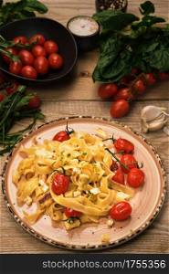 Pasta with grilled cheese slices, frying cherry tomatoes and olive oil. Selective focus, vertical frame. Ingredients for spaghetti on a wooden table. Vegetarian pasta idea