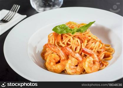 Pasta with jumbo shrimp on a white plate on a black background.