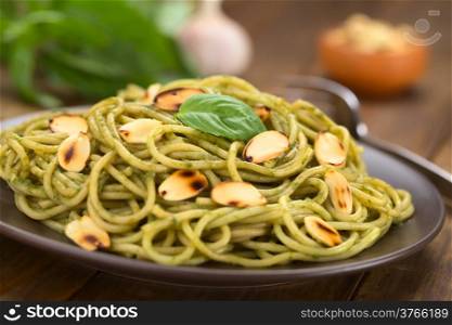 Pasta with pesto made of basil and spinach garnished with roasted almonds served on a brown plate (Selective Focus, Focus on the lower edge of the basil leaf on the dish)