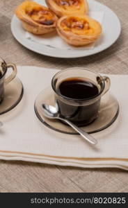 Pasteis de Nata or Portuguese Custard Tarts with black coffee on wooden table.